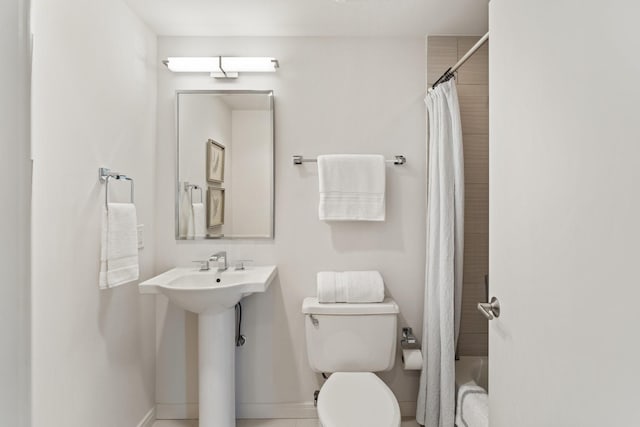 bathroom featuring toilet, shower / bath combo with shower curtain, and baseboards