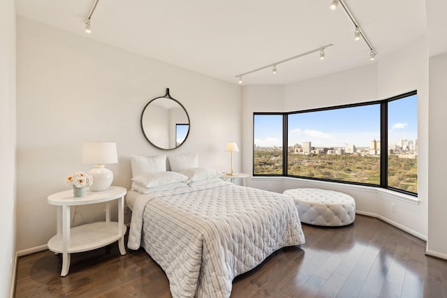 bedroom featuring baseboards, a city view, wood finished floors, and track lighting