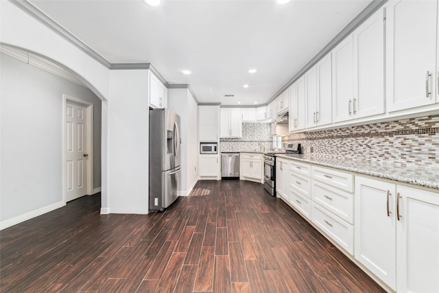 kitchen with dark wood finished floors, decorative backsplash, stainless steel appliances, arched walkways, and white cabinetry