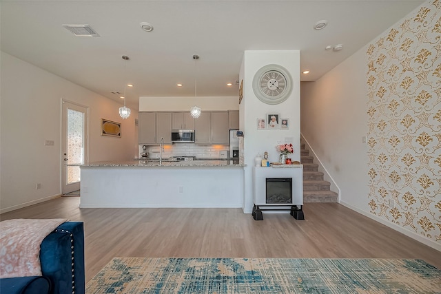 kitchen featuring wood finished floors, gray cabinetry, stainless steel appliances, pendant lighting, and backsplash