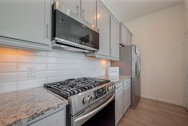 kitchen featuring light stone countertops, baseboards, light wood finished floors, appliances with stainless steel finishes, and backsplash