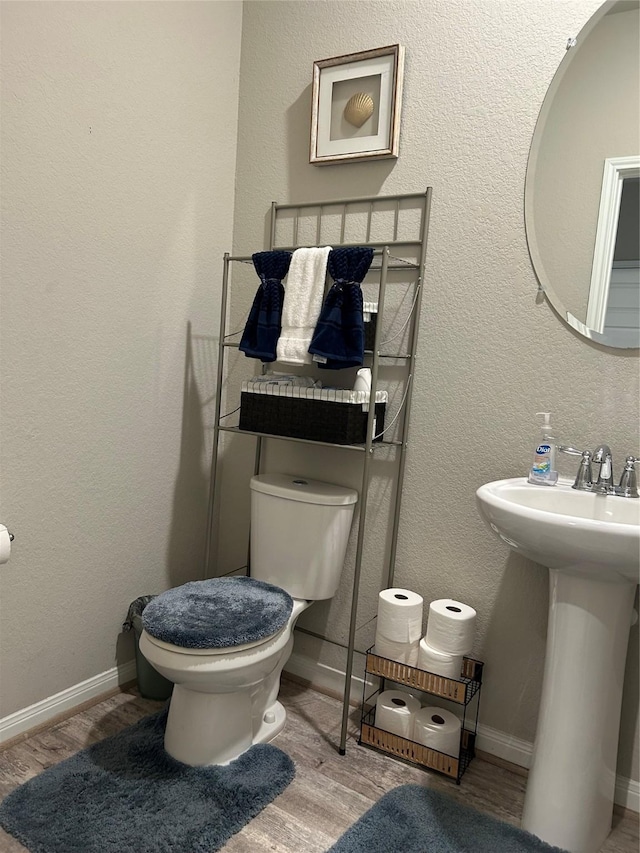 bathroom featuring a textured wall, toilet, a sink, wood finished floors, and baseboards