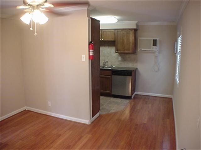 kitchen featuring stainless steel dishwasher, backsplash, light wood-style flooring, and crown molding