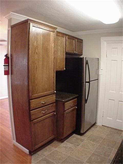 kitchen featuring baseboards, brown cabinetry, dark countertops, freestanding refrigerator, and crown molding