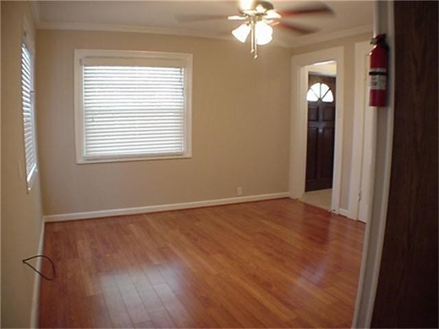 empty room featuring light wood-style floors, plenty of natural light, baseboards, and crown molding