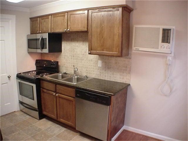 kitchen with dark countertops, appliances with stainless steel finishes, backsplash, crown molding, and a sink