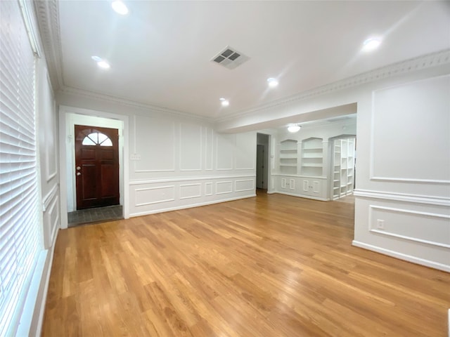 entryway with ornamental molding, light wood-type flooring, visible vents, and a decorative wall