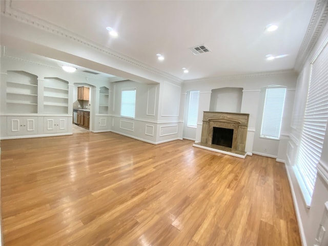 unfurnished living room featuring a decorative wall, a fireplace, visible vents, light wood finished floors, and crown molding