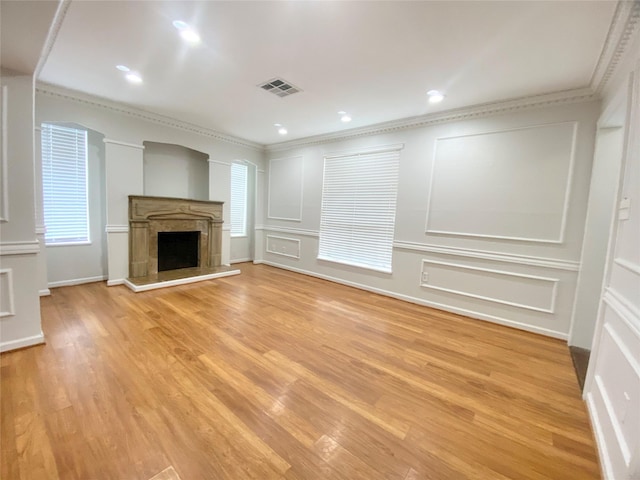 unfurnished living room with a decorative wall, a fireplace, visible vents, ornamental molding, and light wood-type flooring