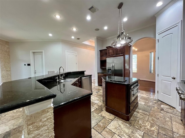 kitchen with visible vents, a large island, a sink, arched walkways, and appliances with stainless steel finishes