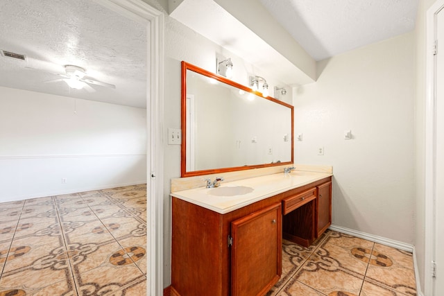 bathroom featuring visible vents, a sink, a textured ceiling, double vanity, and ceiling fan