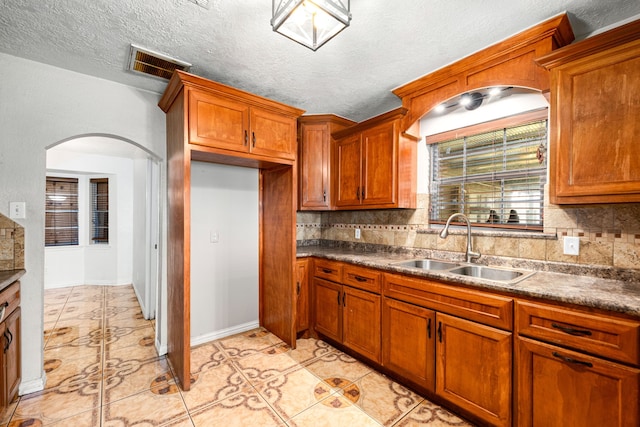 kitchen with brown cabinetry, visible vents, light tile patterned flooring, arched walkways, and a sink