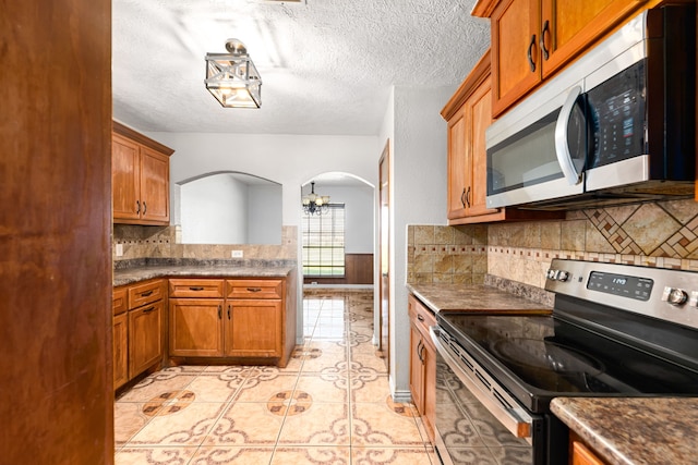 kitchen with light tile patterned floors, stainless steel appliances, arched walkways, and brown cabinetry