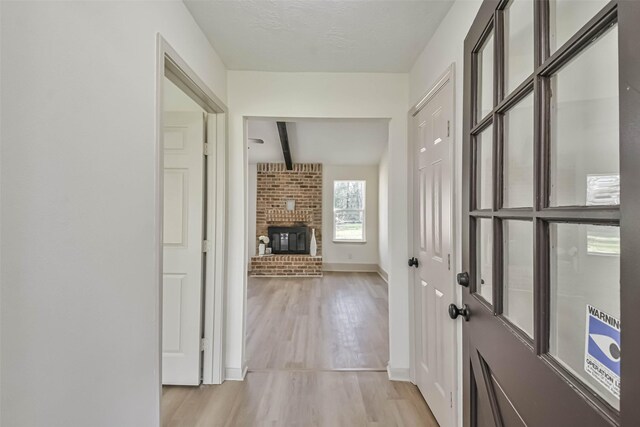 hall featuring beam ceiling, baseboards, and light wood finished floors