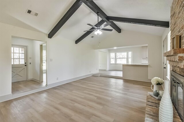 unfurnished living room with lofted ceiling with beams, a fireplace, light wood-type flooring, and a wealth of natural light