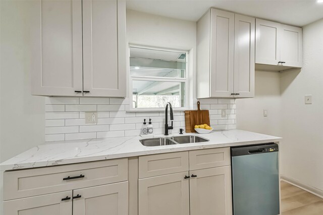 kitchen with backsplash, light stone counters, dishwashing machine, light wood-style floors, and a sink