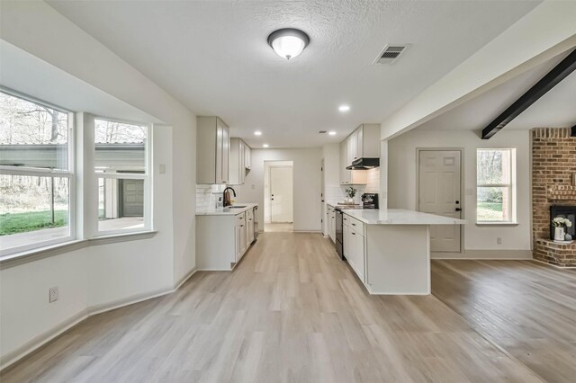 kitchen featuring visible vents, a sink, under cabinet range hood, backsplash, and stainless steel range with electric cooktop