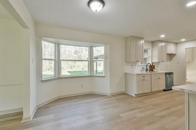 kitchen featuring light wood finished floors, a sink, light countertops, stainless steel dishwasher, and tasteful backsplash