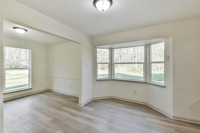 unfurnished room featuring baseboards, a textured ceiling, and light wood finished floors