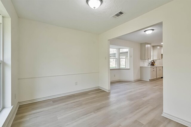 unfurnished room featuring a sink, visible vents, baseboards, and light wood-style floors