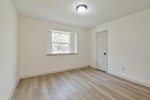 unfurnished room with light wood-type flooring, baseboards, and a textured ceiling