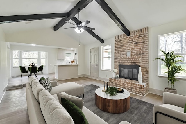 living room featuring light wood finished floors, vaulted ceiling with beams, ceiling fan, baseboards, and a fireplace