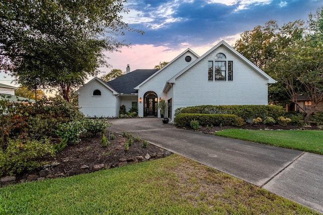 view of front of property featuring concrete driveway, brick siding, and a lawn