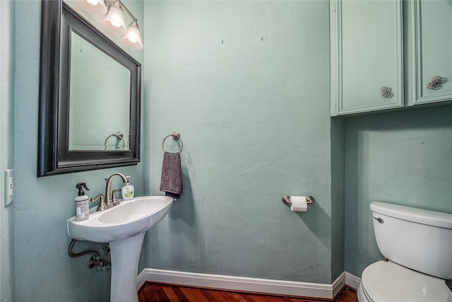 half bathroom featuring wood finished floors, toilet, and baseboards