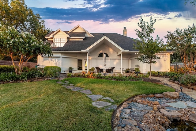 view of front of property with stucco siding, a chimney, a front lawn, and roof with shingles