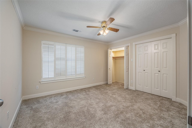 unfurnished bedroom featuring visible vents, carpet, crown molding, a textured ceiling, and two closets