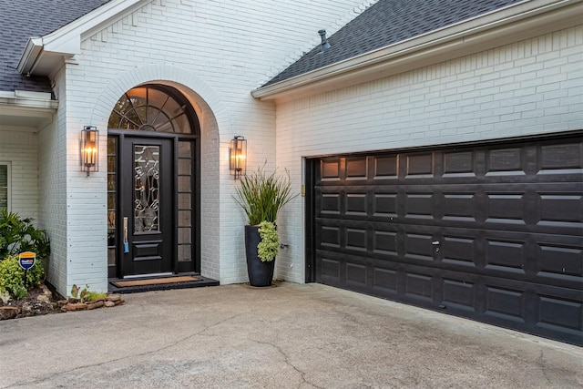 property entrance with brick siding, concrete driveway, and roof with shingles