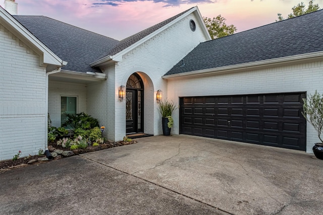 view of front of property featuring driveway, roof with shingles, and brick siding