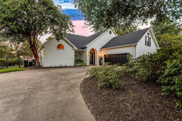 view of front facade featuring brick siding, driveway, an attached garage, and fence