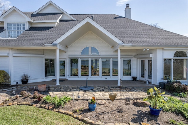 back of property with a patio, a chimney, roof with shingles, french doors, and brick siding