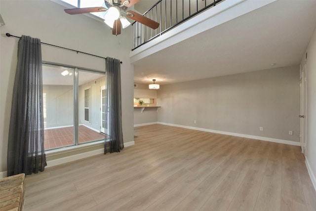 empty room featuring baseboards, a high ceiling, light wood-style flooring, and a ceiling fan