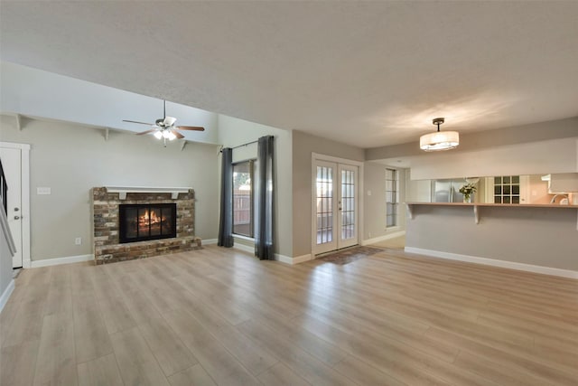 unfurnished living room featuring a brick fireplace, french doors, light wood-type flooring, and baseboards