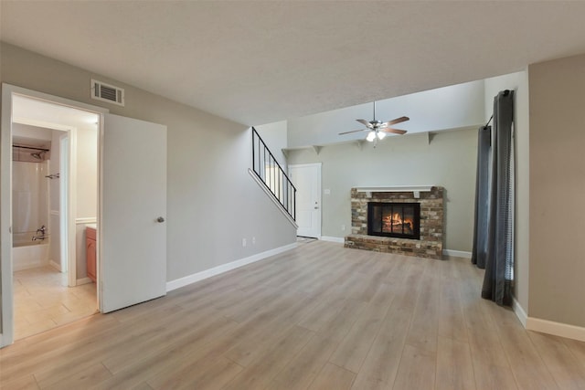 unfurnished living room with visible vents, a brick fireplace, stairs, and light wood finished floors