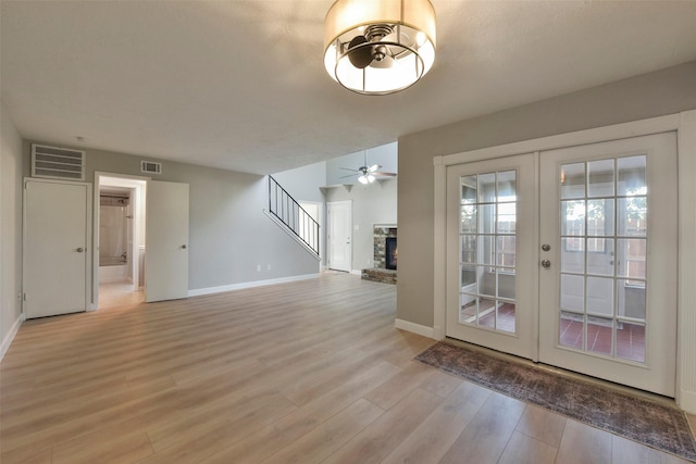 interior space with light wood finished floors, visible vents, stairs, a stone fireplace, and french doors