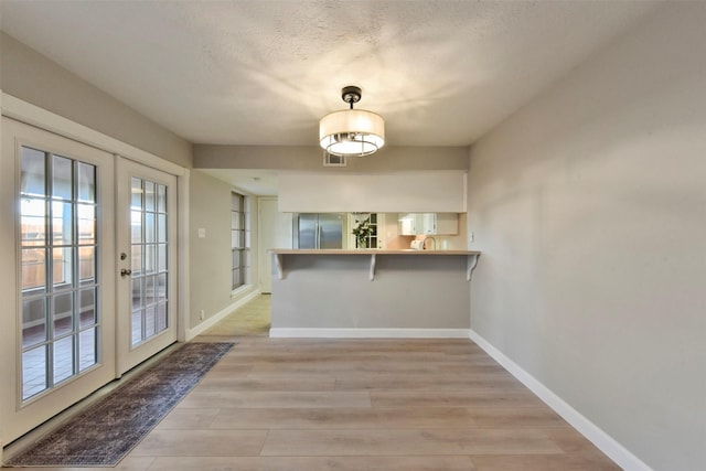 unfurnished dining area featuring french doors, baseboards, a textured ceiling, and light wood-style flooring