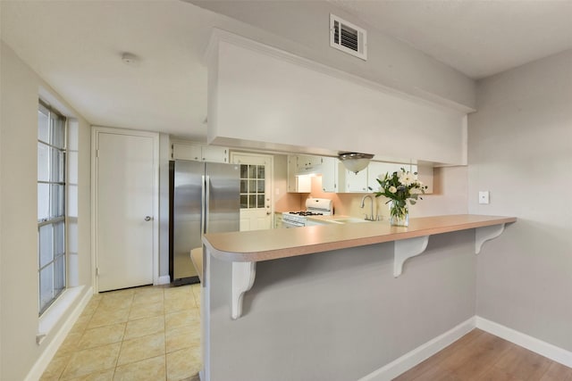 kitchen with visible vents, white range with gas cooktop, a peninsula, freestanding refrigerator, and a sink