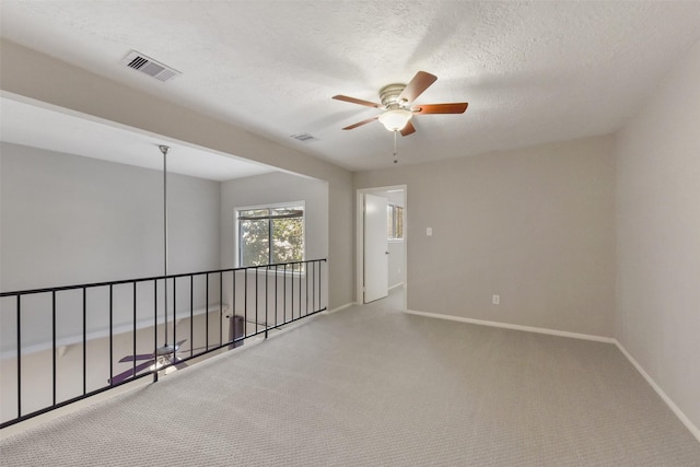 empty room featuring visible vents, baseboards, carpet floors, a textured ceiling, and a ceiling fan