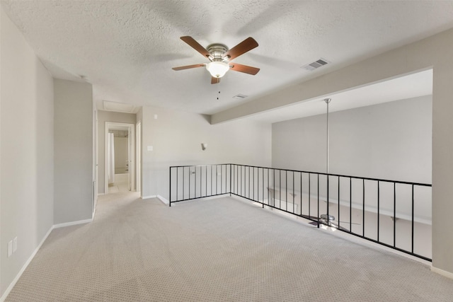 unfurnished room featuring a ceiling fan, carpet, visible vents, and a textured ceiling