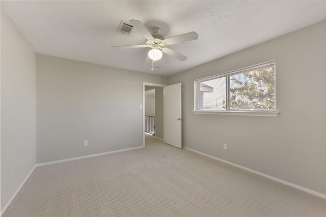 empty room with visible vents, light carpet, a ceiling fan, a textured ceiling, and baseboards