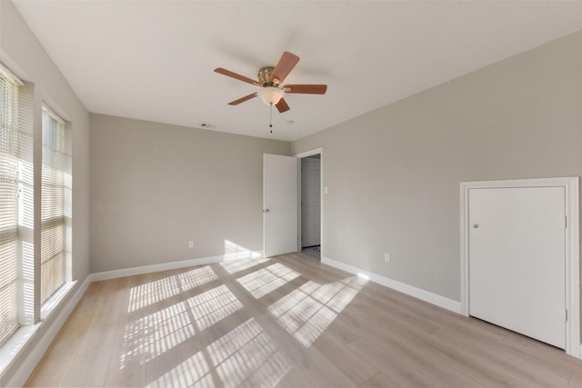 empty room featuring a ceiling fan, visible vents, baseboards, and light wood-type flooring