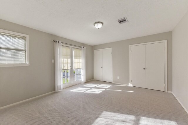 unfurnished bedroom with carpet, baseboards, visible vents, french doors, and multiple closets