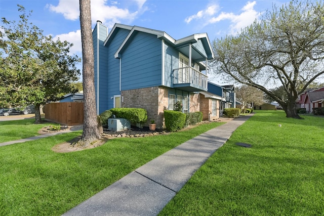 view of property exterior with brick siding, fence, a lawn, a chimney, and a balcony