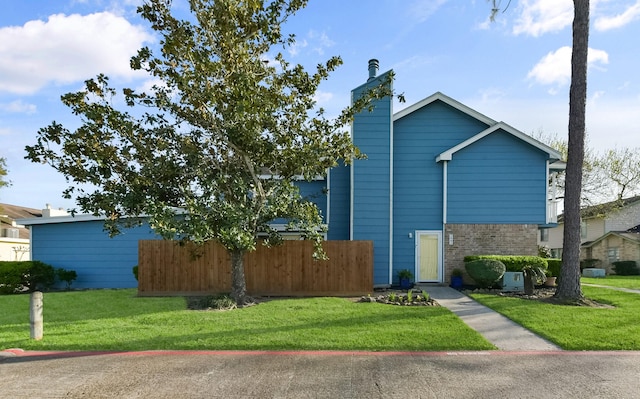 view of side of home featuring a lawn, a chimney, brick siding, and fence