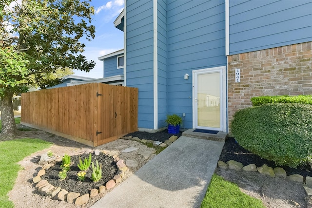 view of exterior entry with fence and brick siding