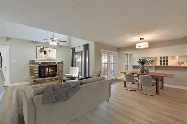 living area with light wood-style flooring, a brick fireplace, baseboards, and french doors