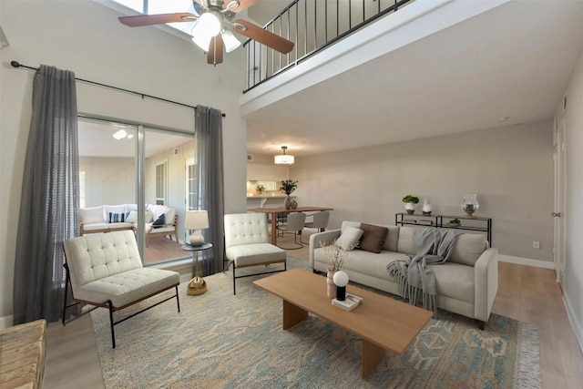 living area with baseboards, a high ceiling, wood finished floors, and a ceiling fan